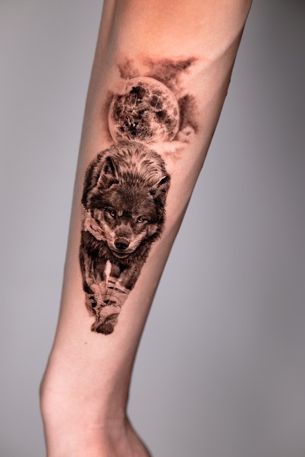A wolf and moon in black and grey, tattooed on the arm