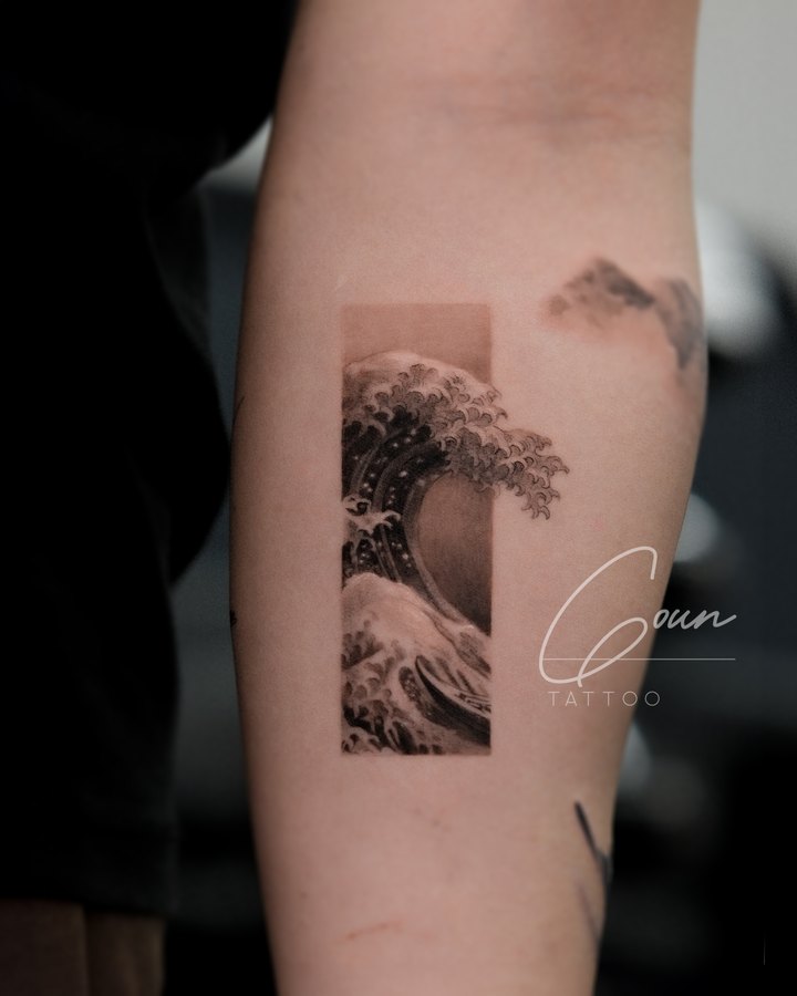 Waves and mountains in black and grey, tattooed on the inner arm